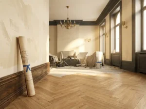 Luxe hotelkamer tijdens renovatie met visgraatparket, sierlijsten, opgerolde bouwtekening en messing armaturen in warm middaglicht.